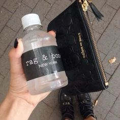 a person holding a water bottle in front of a black purse on the ground with their hand