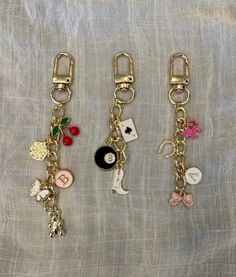 three different key chains with various charms attached to them on a white cloth covered surface