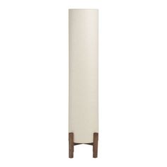 a tall white vase sitting on top of a wooden stand next to a wall mounted light