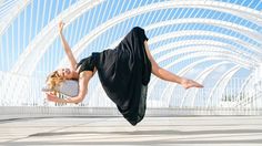 a woman in black dress doing a handstand on concrete floor next to white arches