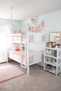 a white bunk bed sitting next to a window with pink curtains and pillows on top of it