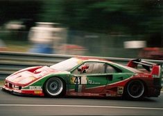 a red and green race car driving on a track with blurry trees in the background