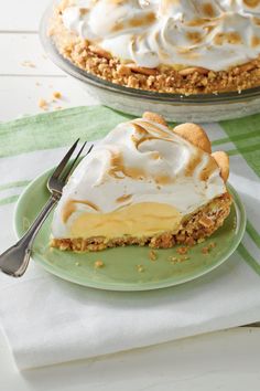 a piece of pie on a green plate next to a fork and glass dish with another pie in the background