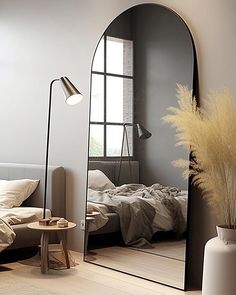 a large mirror sitting on top of a wooden floor next to a white vase filled with flowers