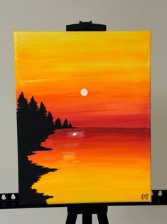 an easel with a painting on it that has a sunset and trees painted on it