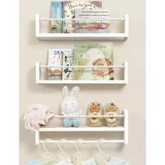 three white shelves with books and stuffed animals hanging from the top, one shelf is filled with baby's clothing