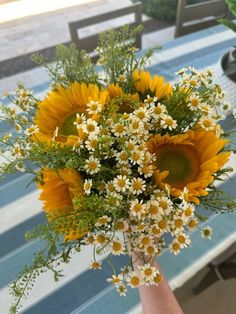 a bouquet of sunflowers and daisies is held by a person's hand