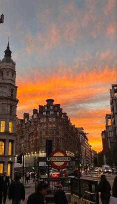 people are walking on the sidewalk in front of some buildings at sunset or sunrise time