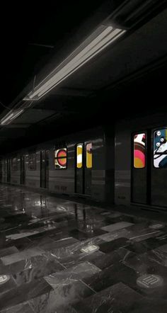 an empty subway station with posters on the wall and tiled floor in front of it