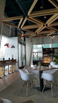 an empty restaurant with white chairs and wooden beams hanging from the ceiling, along with potted plants