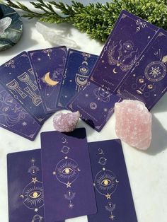 purple tarot cards with gold foil designs on them and a pink rock next to it