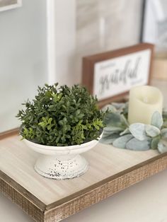 a white bowl filled with green plants on top of a wooden table next to a candle