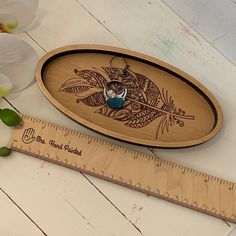 a wooden tray with a blue bead on it next to a ruler and flowers