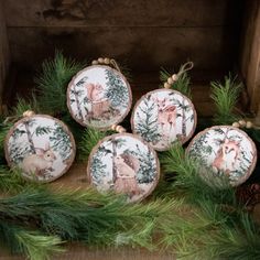 four christmas ornaments with deer and pine needles on them sitting in front of a fireplace