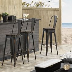 three red metal bar stools sitting on top of a wooden floor next to an ocean