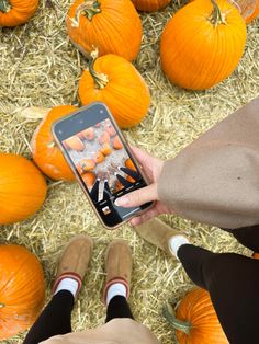 two people holding up a cell phone in front of pumpkins