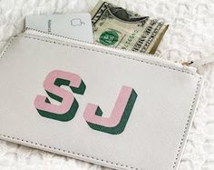 a white wallet with pink and green letters sitting on top of a pile of money