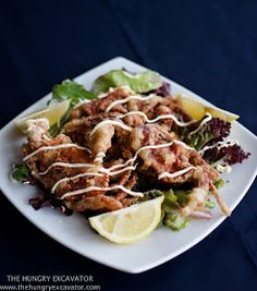 a white plate topped with meat and salad next to a slice of lemon wedges