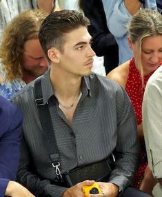 a man sitting in front of a group of people wearing suspenders and holding a cell phone