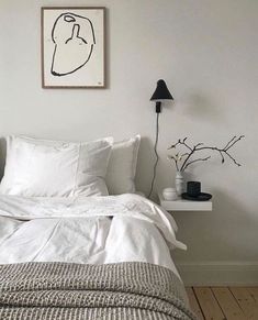 a bed with white sheets and pillows next to a black lamp on a wooden floor