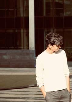 a young man standing in front of a building wearing a white sweater and black pants