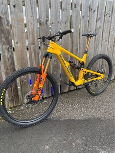 a yellow mountain bike parked next to a wooden fence