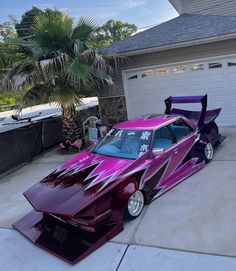 a purple car is parked in front of a garage with palm trees and a house behind it