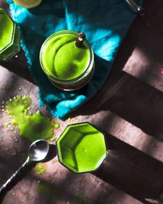 three jars filled with green liquid on top of a wooden table next to two spoons