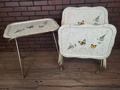 two white trays with butterflies on them sitting next to each other in front of a brick wall