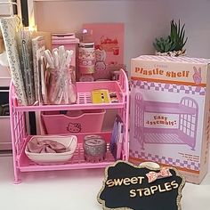 a pink shelf filled with lots of stuff next to a cardboard box and candle holder