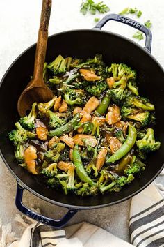 broccoli and chicken stir fry in a pan with a wooden spoon on the side