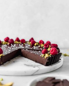 a chocolate cake topped with raspberries on top of a white plate next to bananas