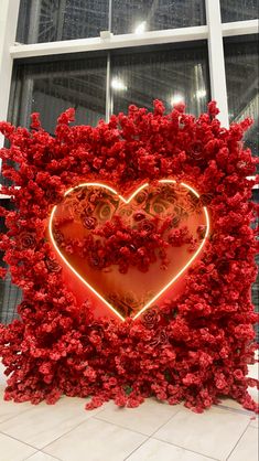 a red heart shaped sculpture in front of a window with flowers on the outside and inside