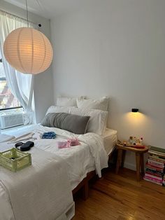 a white bed sitting next to a window in a bedroom under a light hanging from the ceiling