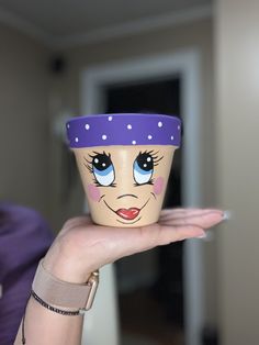 a woman holding up a cup with a face painted on it's front and side