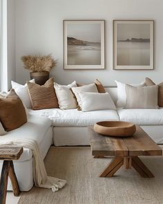 a living room with white couches and pillows on top of the couch, two pictures above them