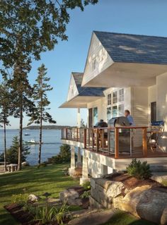 two people are sitting on the porch of a house overlooking the water and boats in the distance