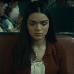 a woman with long hair sitting in a booth looking at the camera while wearing a brown cardigan