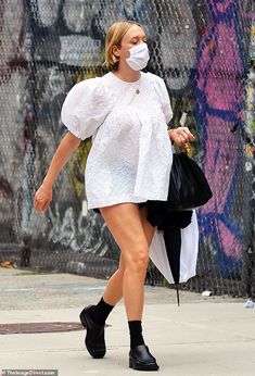 a woman walking down the street wearing a face mask and carrying a black bag in her hand