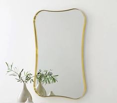 a gold framed mirror on a wall next to two vases with plants in them