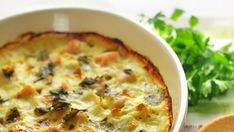 a casserole dish with cheese and vegetables in it on a table next to parsley