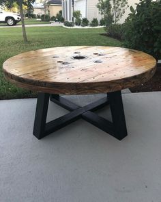 a round wooden table sitting on top of a cement floor in front of a house