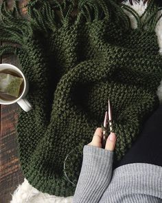 a person holding a pair of scissors next to a cup of coffee on top of a blanket