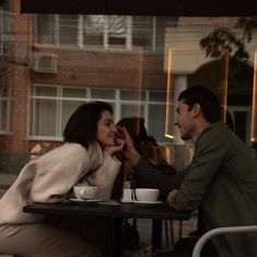 a man and woman sitting at a table in front of each other with coffee cups