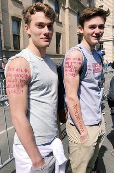 two young men standing next to each other with tattoos on their arms