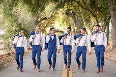 a group of men in blue suits and bow ties walking down a road with trees behind them