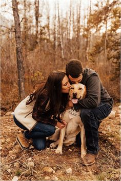 a man and woman kissing their dog in the woods