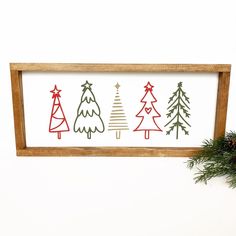 a wooden frame with christmas trees painted on it and pine branches in the corner next to it