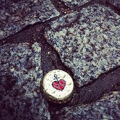 a bottle cap with a heart painted on it laying on the ground next to pavement