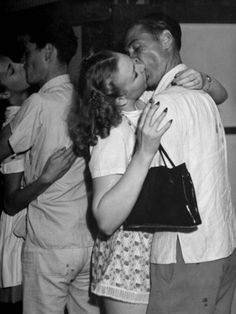 a man and woman kissing while standing next to each other in front of some people